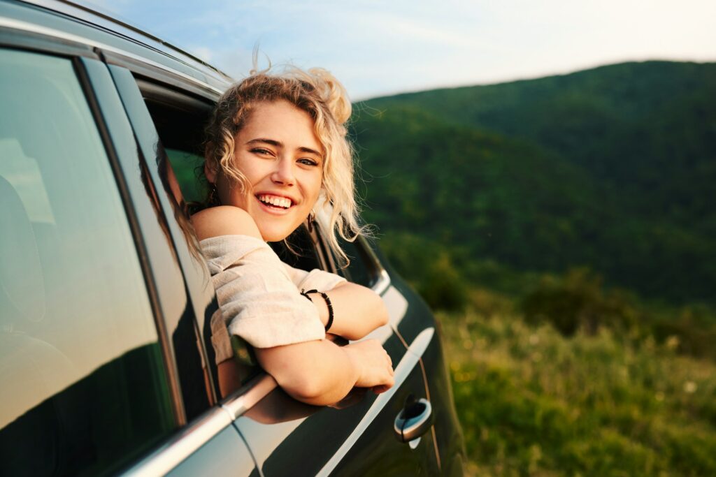 Happy young blonde woman leaning out of the car window enjoying nature