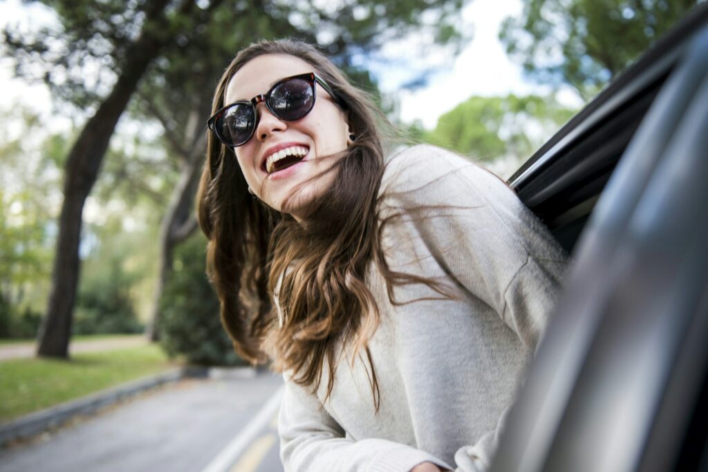 Happy young woman on road trip leaning out of car window